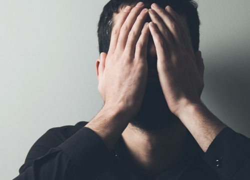 Man dealing with depression, covering his face with his hands